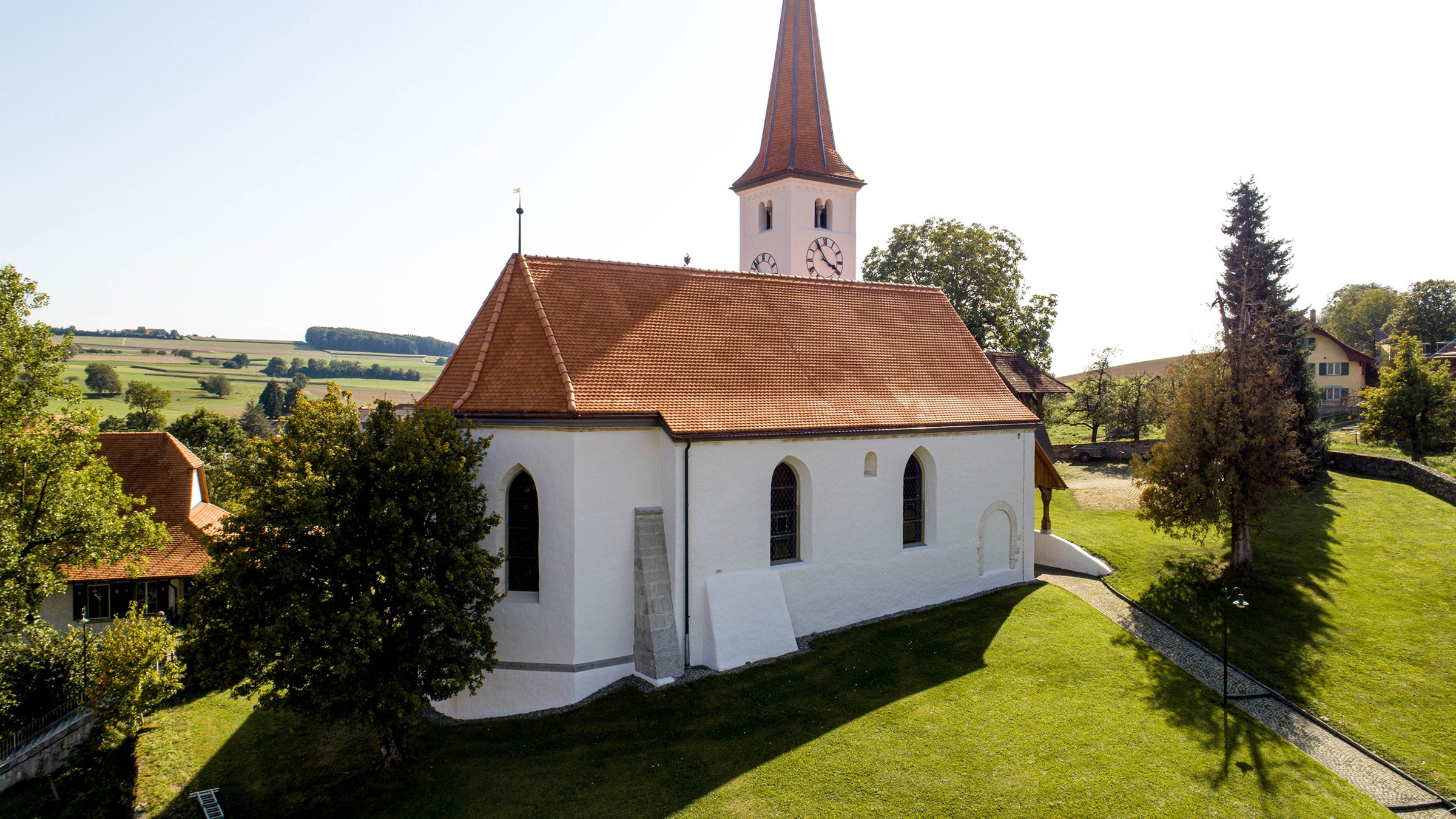 Drohnenaufnahme der Kirche Oberwil, die mit 24'400 Stück Biberschwanzziegel Berner Biber, spitz, naturrot von Gasser Ceramic eingedeckt ist.